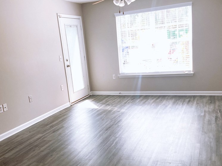 empty living room in an apartment in Fayetteville with large window ceiling fan and wood-look floors